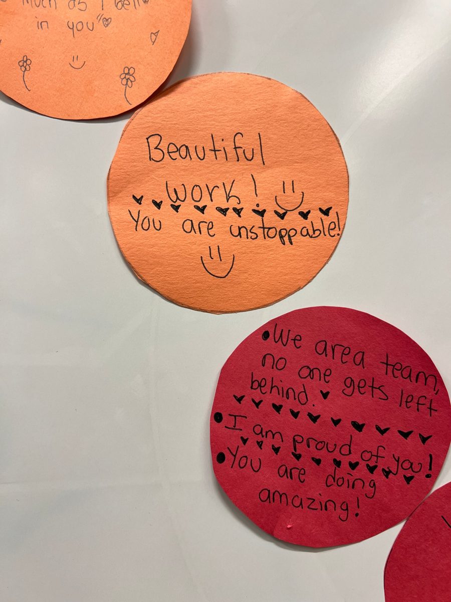 Close-up of two paper circles. The orange circle reads: Beautiful work! You are unstoppable! The red circle reads: We are a team, no one gets left behind. I am proud of you! You are doing amazing! Both are decorated with hearts and smiley faces.